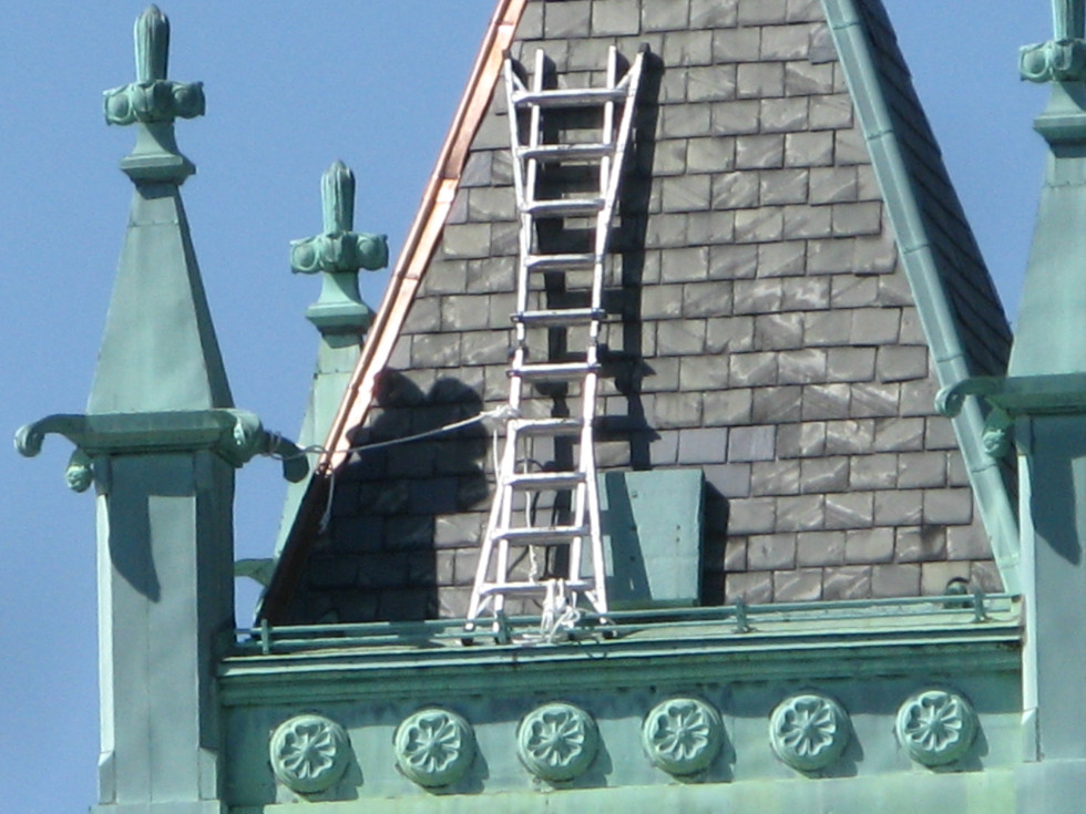 Shinny new copper cap flashing applied to a steep sloped slate roof on a church steeple.
